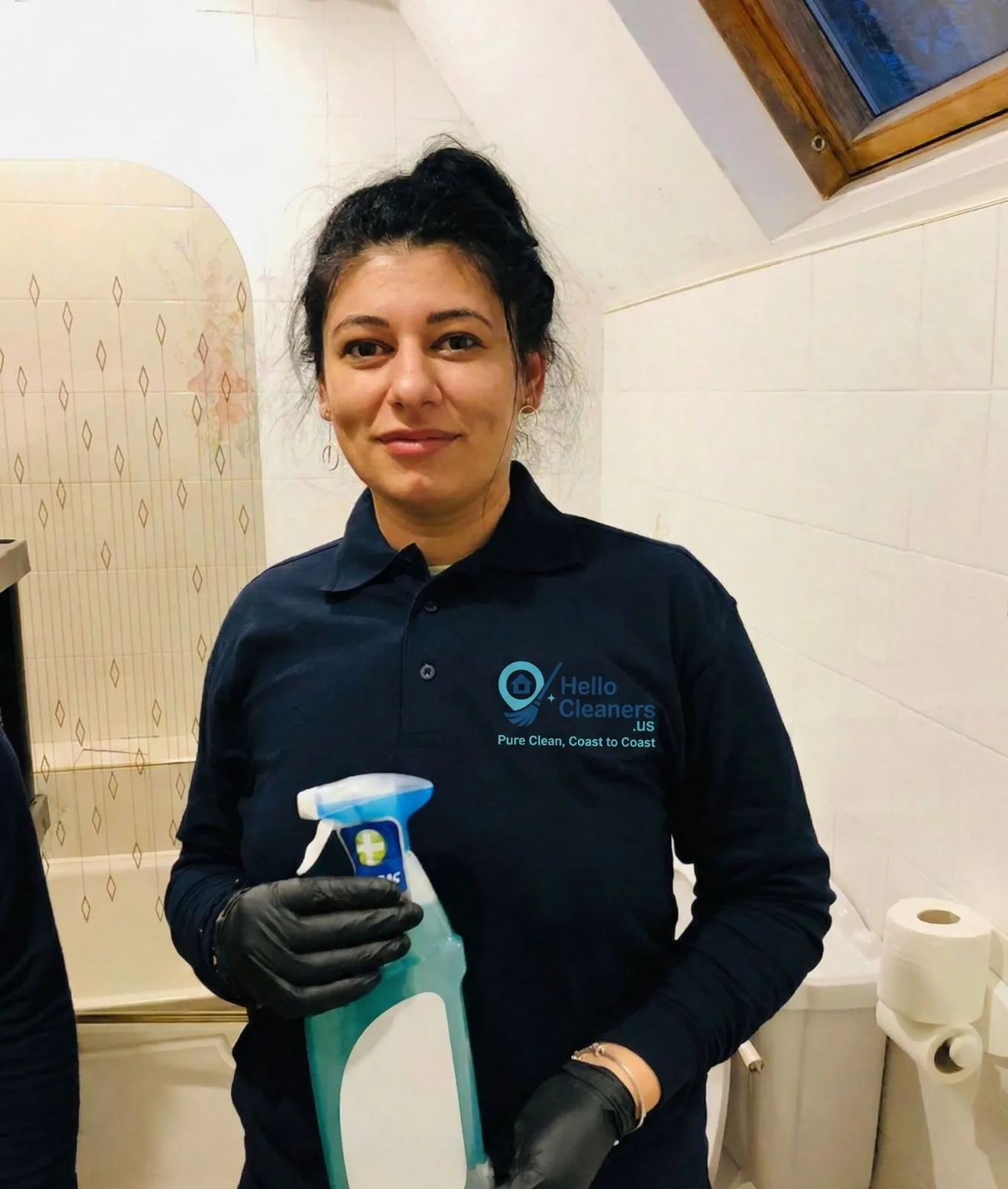 Hello Cleaners cleaner in a branded polo shirt disinfecting a bathroom
